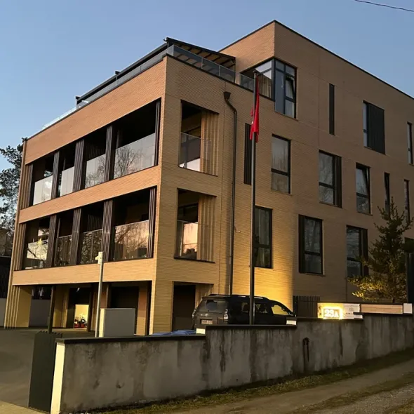Modernaus keturaukščio pastato fasadas iš šilto ochros atspalvio ilgų klinkerinių plytų vakare