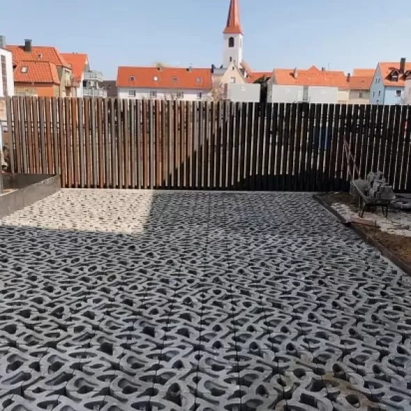 Ornamentinės struktūros ažūrinių eko betoninių trinkelių klojamas kiemo grindinys šalia medinės tvoros