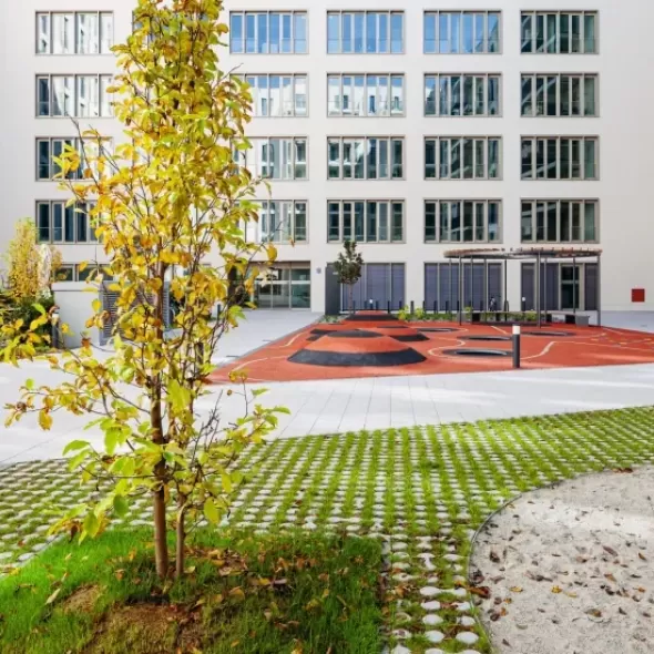 Organiškų vingiuotų formų ažūrinių eko betoninių trinkelių ornamentinis grindinys su žaliuojančia veja daugiabučių kieme
