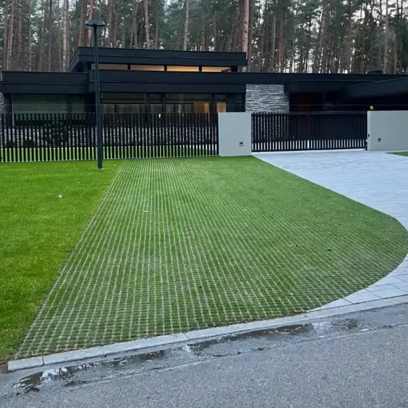 Kvadratinių tinklinių ažūrinių betoninių trinkelių su žaliuojančia veja tvarus ir estetiškas grindinys moderniame kieme 