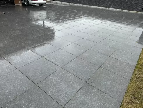 Tamsiai pilkos antracito spalvos šlapios lauko kiemo aikštelės keraminių betoninių plytelių danga prie žolės vejos